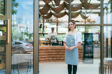 Hand of coffee shop staff woman wearing apron turning open sign board on glass door in modern cafe,...