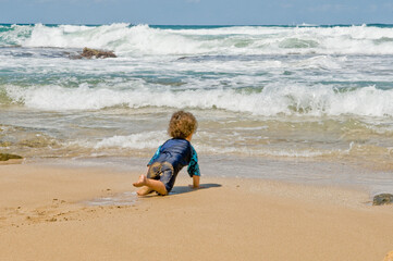 A child crawls along the sand towards the sea waves