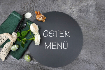 Tischdekoration zu Ostern mit Ostereiern und dem Text Ostermenü auf einer Schieferplatte.