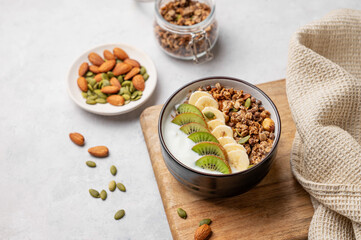Muesli with yogurt, banana and kiwi in a bowl on a cutting board on a light background.