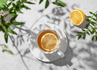 A cup of tea with lemon and green branch on a white table.  Breakfast detox and healthy concept.