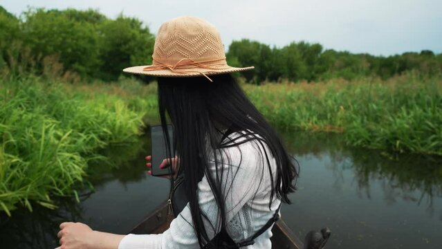 girl in a boat floating on the floodplain of the river, taking a picture of the landscape on her phone