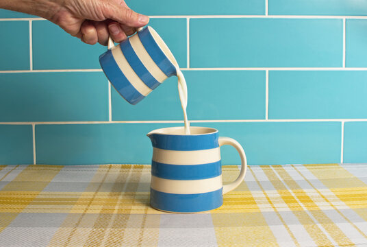 Milk image with a blue and white jug pouring fresh milk into another similar jug. Blue white and yellow colours. Dairy produce concept.
