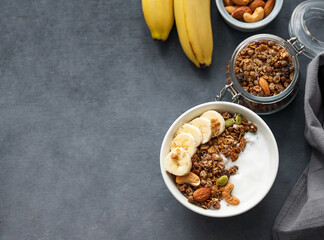 Healthy breakfast. Flat lay of homemade granola with banana and nuts in a bowl on a dark  background.