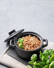 Buckwheat porridge in a black pan on a light background with fresh herbs.