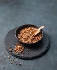 Raw buckwheat grains  in a wooden bowl on a board on a dark background.
