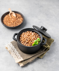 Buckwheat porridge with fresh herbs in a black pan on a light background with raw grains.