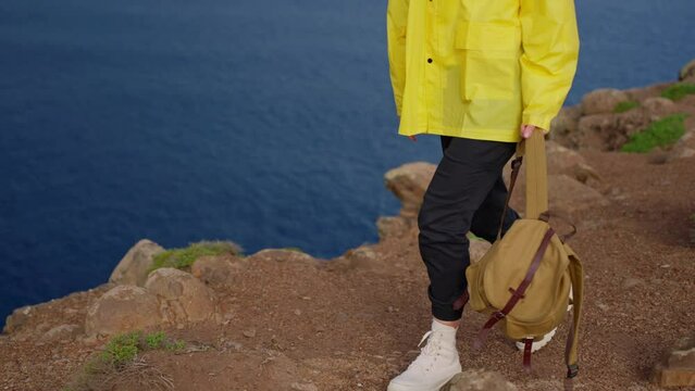 Attractive traveling woman in a yellow jacket and backpack looking at windmills in field 