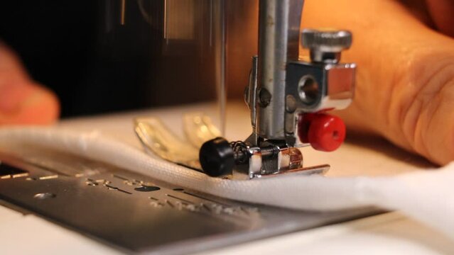 A seamstress sews a stitch on fabric using an electric sewing machine, close up.