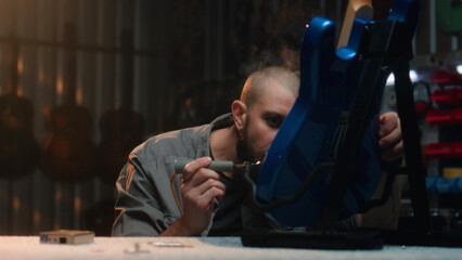 Professional carpenter solders guitar strings using soldering iron. Male craftsman makes wooden...