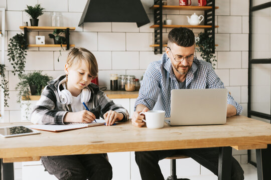 family dad young man with phone and son teenage cute boy with tablet and headphones doing homework sit at table in cosy apartment, quality time with your family, gadget addicted, education