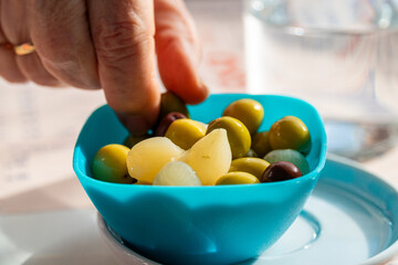 A person picks olives from a bowl of pickled vegetables. 
