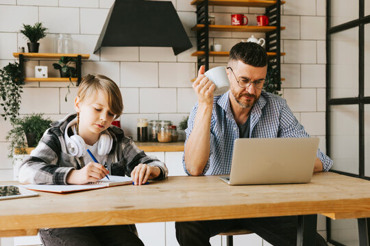 family dad young man with phone and son teenage cute boy with tablet and headphones doing homework sit at table in cosy apartment, quality time with your family, gadget addicted, education
