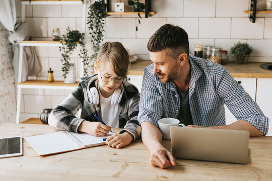 family dad young man with phone and son teenage cute boy with tablet and headphones doing homework sit at table in cosy apartment, quality time with your family, gadget addicted, education