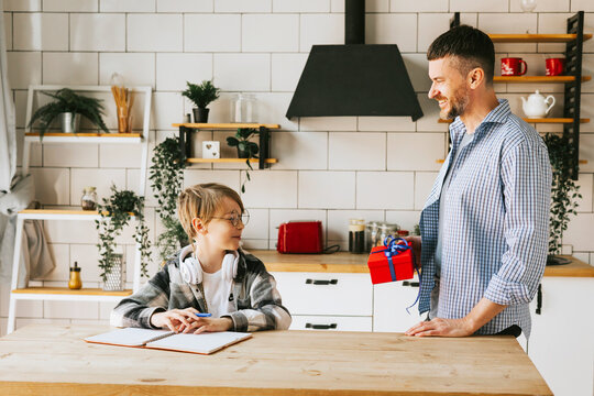family dad young man and son teenage cute boy doing homework sit at table in cosy apartment, quality time with your family, dad gives the child a gift