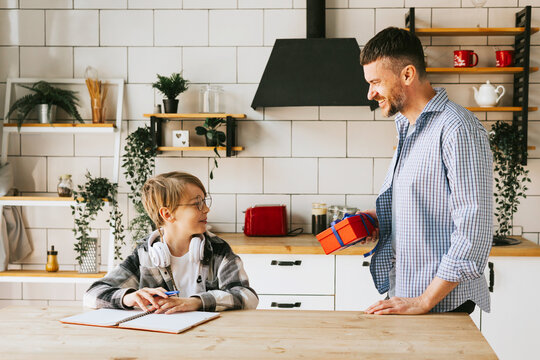 family dad young man and son teenage cute boy doing homework sit at table in cosy apartment, quality time with your family, dad gives the child a gift