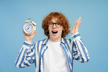 Shocked emotional boy holding an alarm clock and screaming isolated
