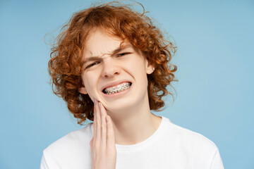 Sad ginger boy holding hand on his cheek having a toothache, need medical treatment