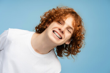 Portrait of smiling confident boy, curly red haired teenager with dental braces looking at camera