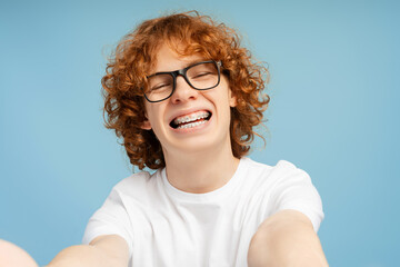 Portrait of smiling boy, curly teenager with dental braces looking at camera making selfie