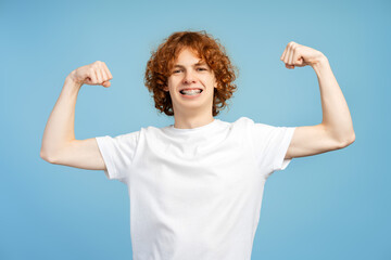 Portrait of smiling strong teenage boy wearing stylish white t shirt showing muscles looking at...