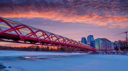 Winter sunrise over the Peace Bridge leading to downtown in Calgary with frozen and snow-covered Bow River. - 741878859
