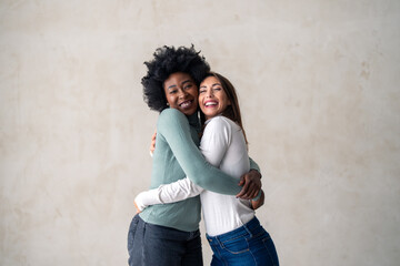 Two best friends smiling while embracing each other in a studio. Happy young women enjoying...
