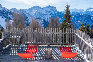 Empty red deck chairs and winter landscape with snow covered Dolomites in Kronplatz, Italy