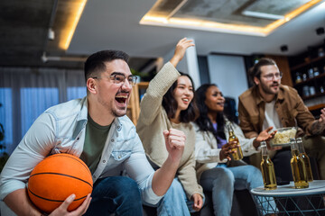 Multiracial group of friends watching basketball game, drinking beer and cheering.