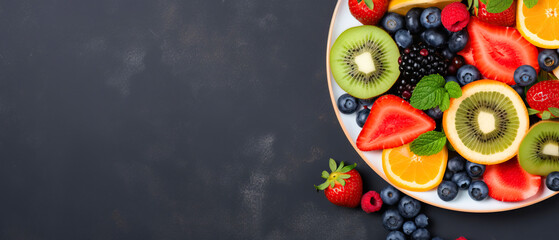 Obraz na płótnie Canvas Web banner with fresh summer salad of various fruits and berries. Kiwi, orange, strawberry and blueberry on a plate decorated with mint on a table top view, free space for text