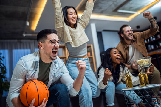 Multiracial group of friends watching basketball game, drinking beer and cheering.