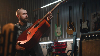 Male carpenter inspects acoustic guitar in detail. Professional craftsman makes wooden musical...