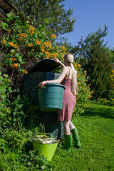 A young girl puts vegetable waste into a compost bin in the garden in the summer.