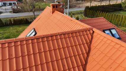 Pomarańczowy dach budynku kryty blachodachówka, okna dachowe, komin, widok z drona.