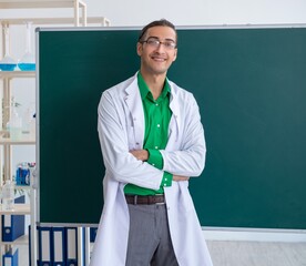 Young male chemist teacher in front of blackboard