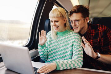 A happy young travelers sitting in a train and having video call on laptop.