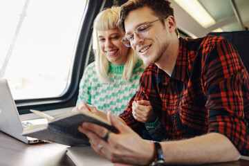 A young couple traveling with train and using laptop and reading book.