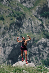 A sportswoman is achieving a goal and standing on a cliff in mountains.