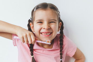 close-up portrait of a child, a 6-year-old girl with fallen milk teeth, smiling, grimacing and holding a toothbrush with toothpaste in her hands on white background - obrazy, fototapety, plakaty