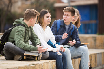 Group of positive teenagers having fun together sitting on steps outdoors at big city