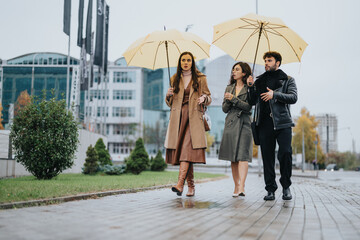 A group of three young adults are strolling through a wet urban landscape, carrying yellow...