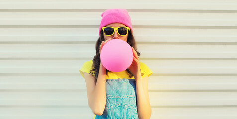Fashion portrait of stylish cool young woman inflating chewing gum or balloon in colorful clothes