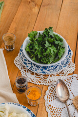 bowl of kale over flower plate and vintage knitted table runner with vintage spoon and spices on wooden table 
