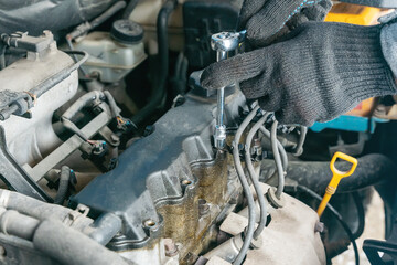 Mechanic's hands unscrew the valve cover of an internal combustion engine to replace the gasket