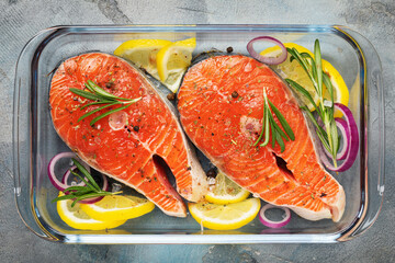 Red fish steaks with various ingredients in a glass baking dish on the table, top view of fresh...