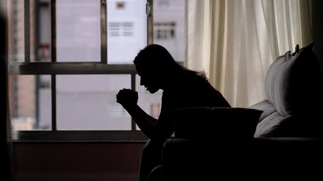 Sillhouete of hopeful young woman clasping hands in prayer asking for blessing. Religion and faith concept
