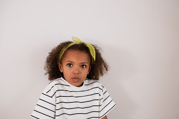 A contemplative young mixed race girl with curly hair and a lime headband on a white background is...