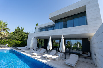 Modern upscale villa with pool, parasols and sunbeds. Modern cubic villa.