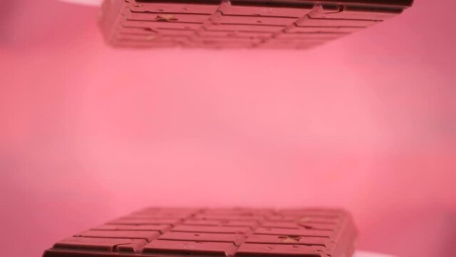 Close-up a milk ruby chocolate bar with chunks of nuts almonds and strawberry, displayed against a pink background is placed on a reflective surface on March 8 Woman's Day