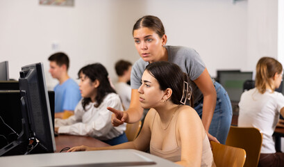 Portrait of young female student helping her female friend studying in computer class using pc in...